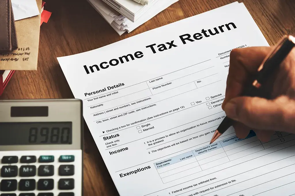 A hand filling in a printed tax return form beside a calculator